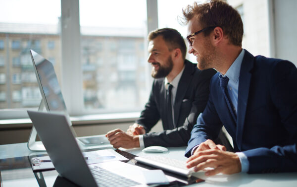Smiling businessman and his colleague looking at computer monitor at meeting